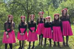 Na-wspolnym-zdjeciu-widac-7-uczestniczek-wystepow-na-Folk-Festiwalu.-Dziewczeta-sa-spodniczkach-czarnych-bluzkach.-We-wlosy-maja-wpoleciony-rozowy-wianek