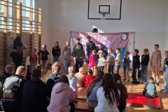Grupa-uczniow-aktywnie-uczestniczy-w-spektaklu.-Uczestnicy-stoja-jeden-obok-drugiego-naprzeciwko-widowni
